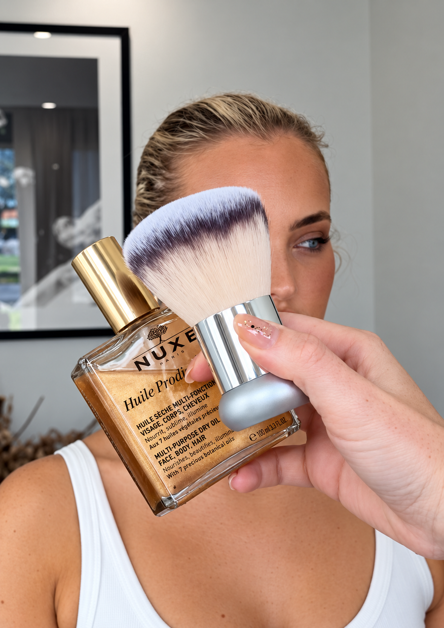 A model holding The Glow Brush against her cheek to showcase its soft bristles and glossy skin finish