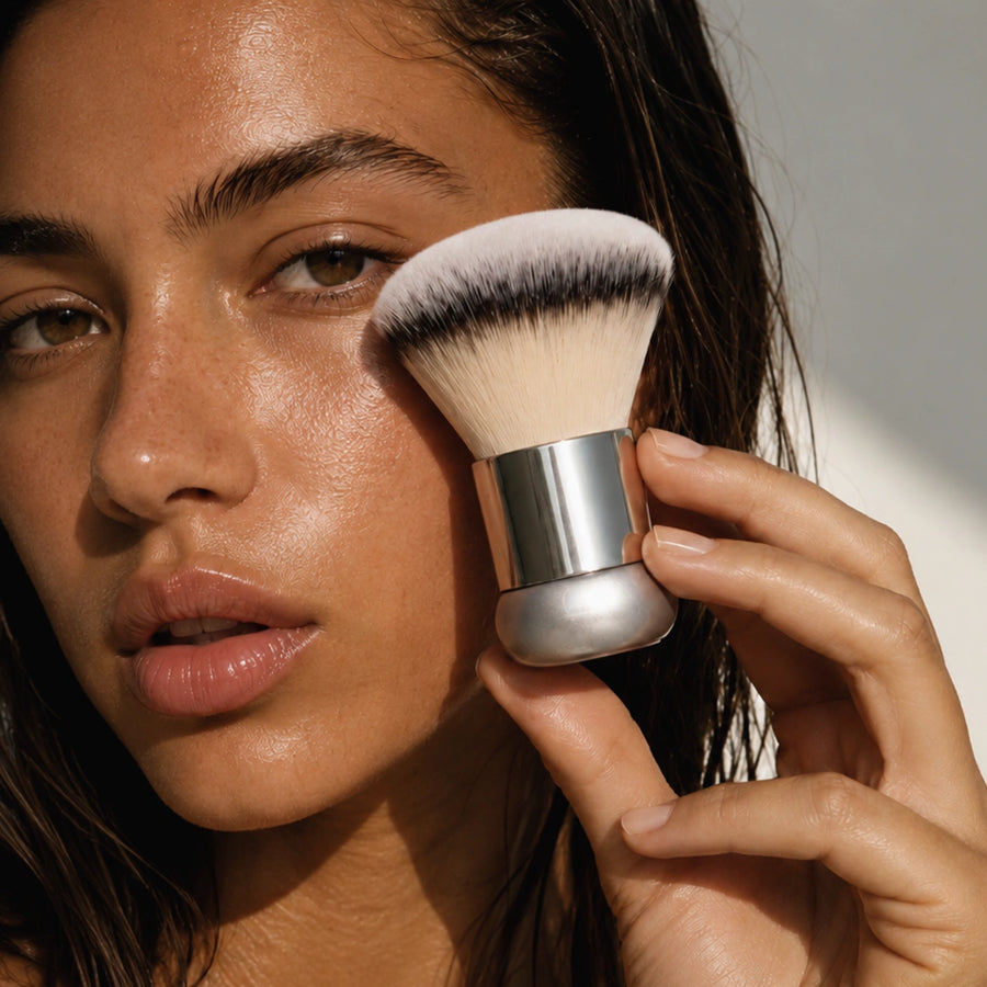 A close-up of a tinted body lotion or glow cream being pumped directly onto the soft, dense bristles of The Glow Brush